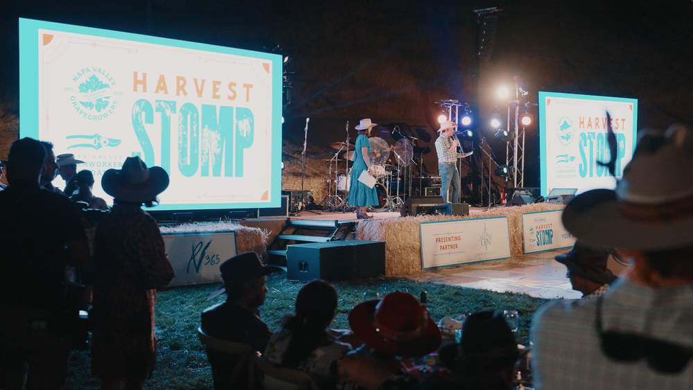 Outdoor nighttime event setup with illuminated signs and vehicles visible in the darkness.
