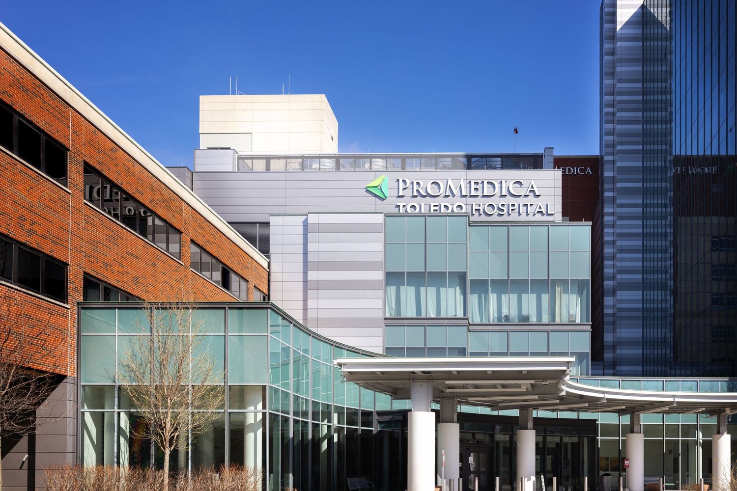 Modern office buildings with glass facades and brick exteriors form a connected commercial complex on a sunny day.