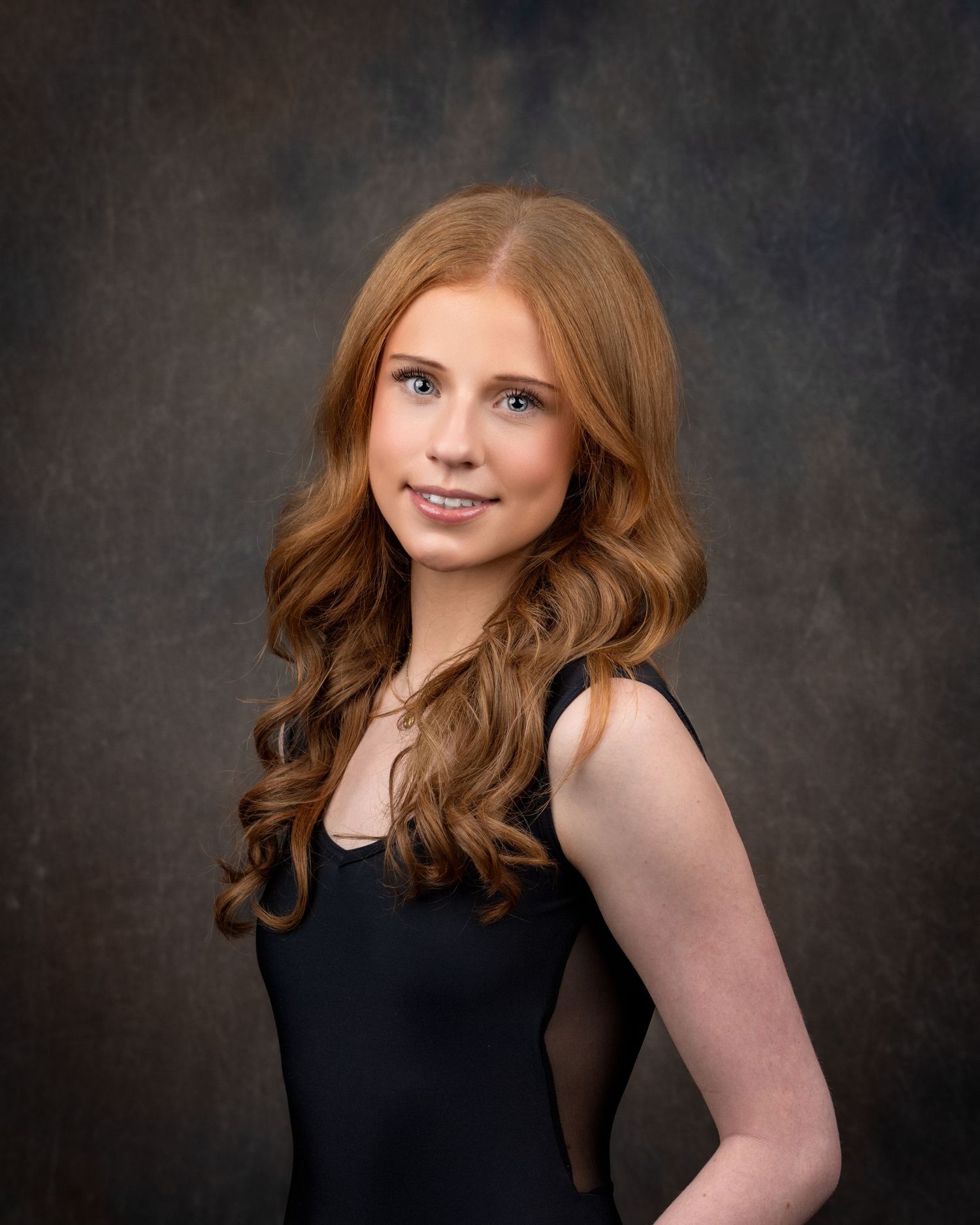 Professional headshot portrait of someone in a black blazer and blue top against a dark gray background.