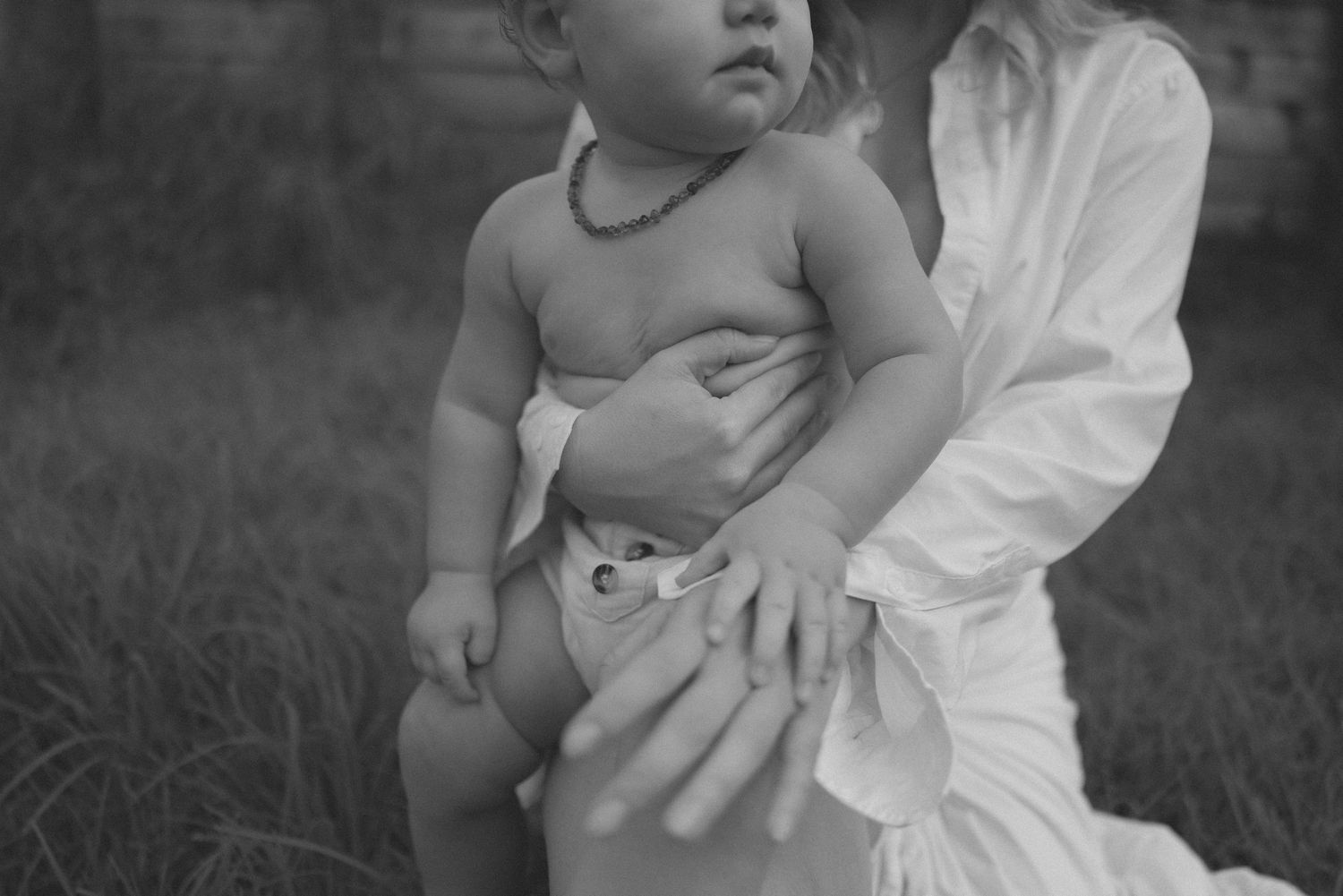 Black and white close-up of baby with necklace held by woman in white dress in New Zealand.