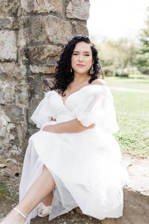 A dreamy portrait in white dress sitting against a stone wall with natural outdoor lighting.