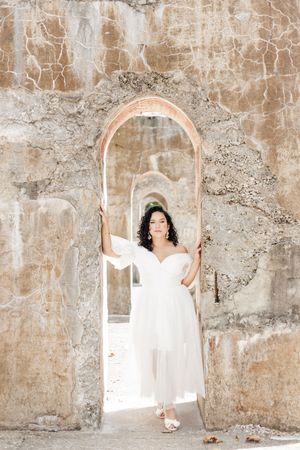Ethereal white dress photoshoot with vintage arched stone wall backdrop.
