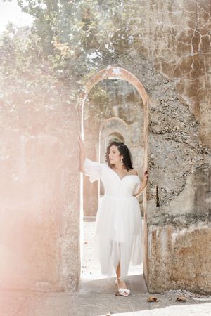 A person in a flowing white dress poses gracefully against a weathered stone wall in an artistic photo series.