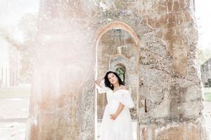 Maternity portrait session featuring white dress against textured stone wall background.