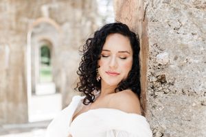 A bride in a white dress poses against a stone wall backdrop in an elegant outdoor setting.