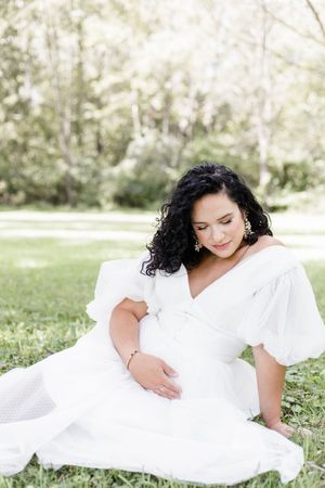A person in a flowing white dress lies gracefully on lush green grass in a dreamy outdoor setting.