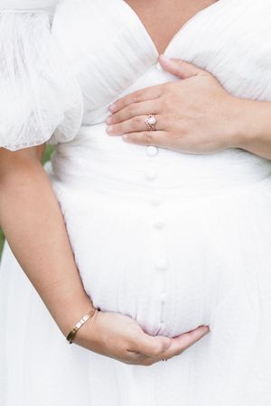 Close-up shots of hands cradling a pregnant belly in a white maternity dress.