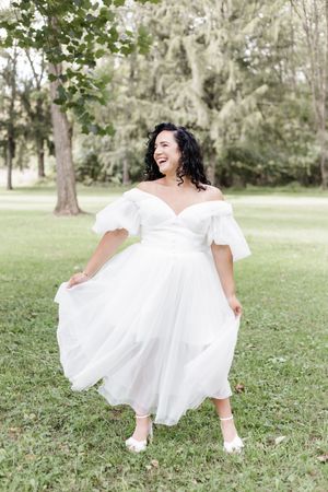 A flowing white dress twirls gracefully on green grass in a sunlit garden setting.