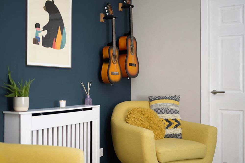 Modern living room corner with yellow armchair, wall-mounted guitars, and teal accent wall against white radiator cover.
