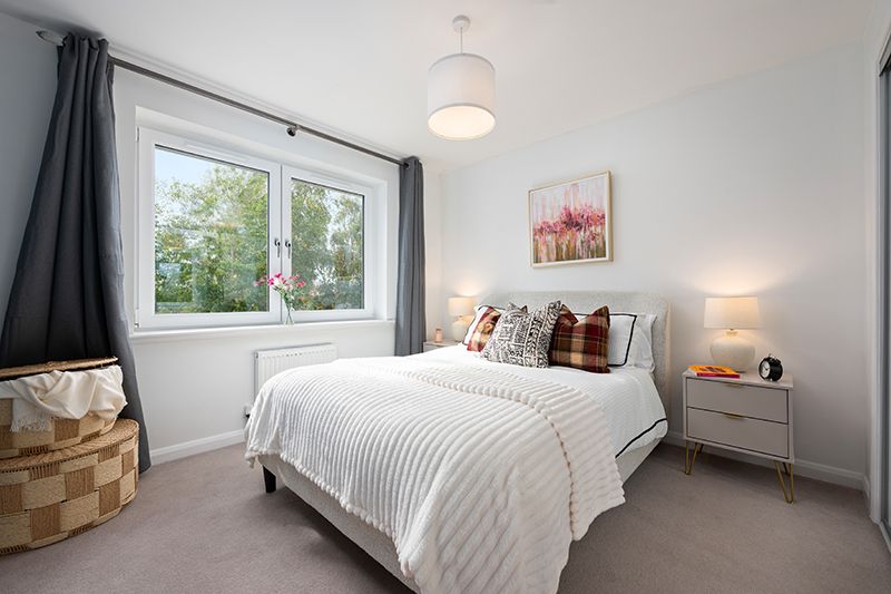 Modern white bedroom with clean bedding, natural light from windows, and minimalist decor in a bright interior space.