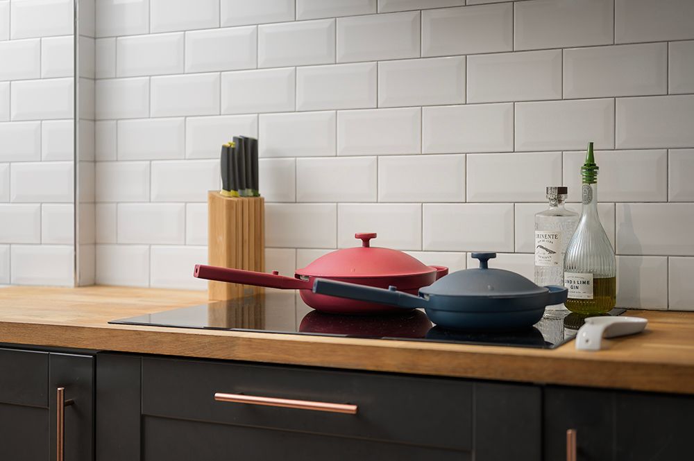 Red and gray cast iron cookware displayed on wooden countertop against white subway tile backsplash in modern kitchen.