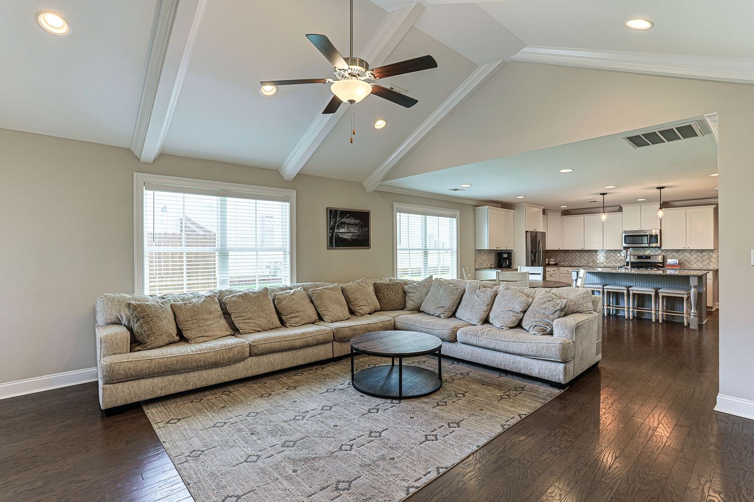 Modern open concept living room with vaulted ceiling, ceiling fan, neutral sectional sofa and connected kitchen space in Dothan, AL