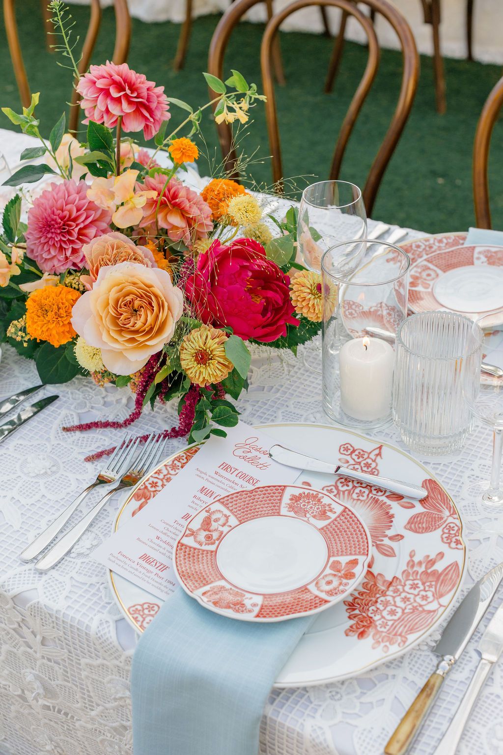 Beautiful floral centerpiece arrangement with vibrant red and pink dahlias displayed on wooden table at outdoor event.