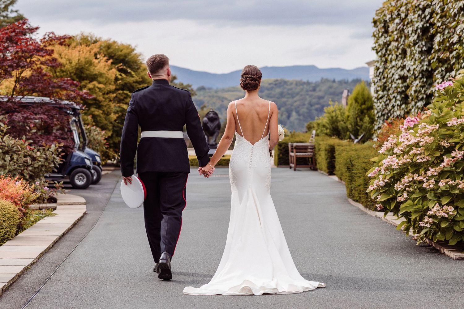 Couple walks down garden path overlooking mountain vista in formal wedding attire on their special day.