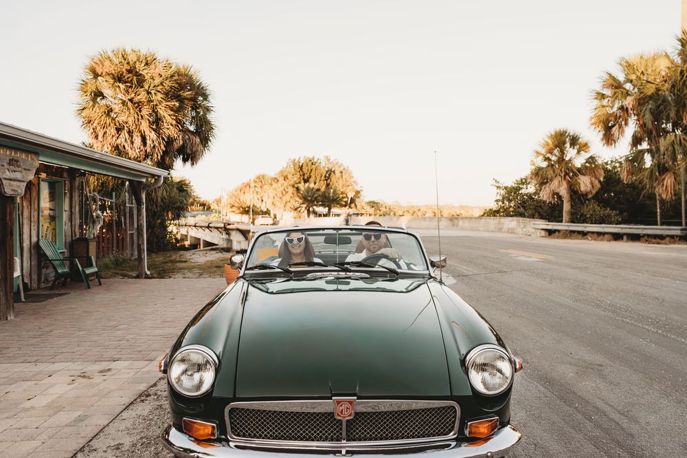 Engaged couple posing with a classic vintage car during golden hour in Aripeka Florida