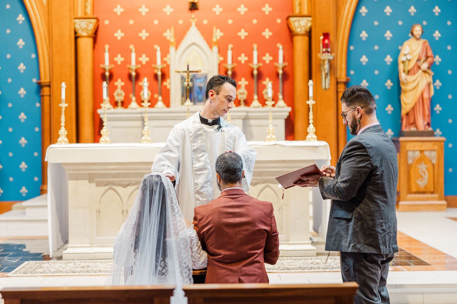 People gather at a church altar with ornate blue and orange patterned walls in the background.