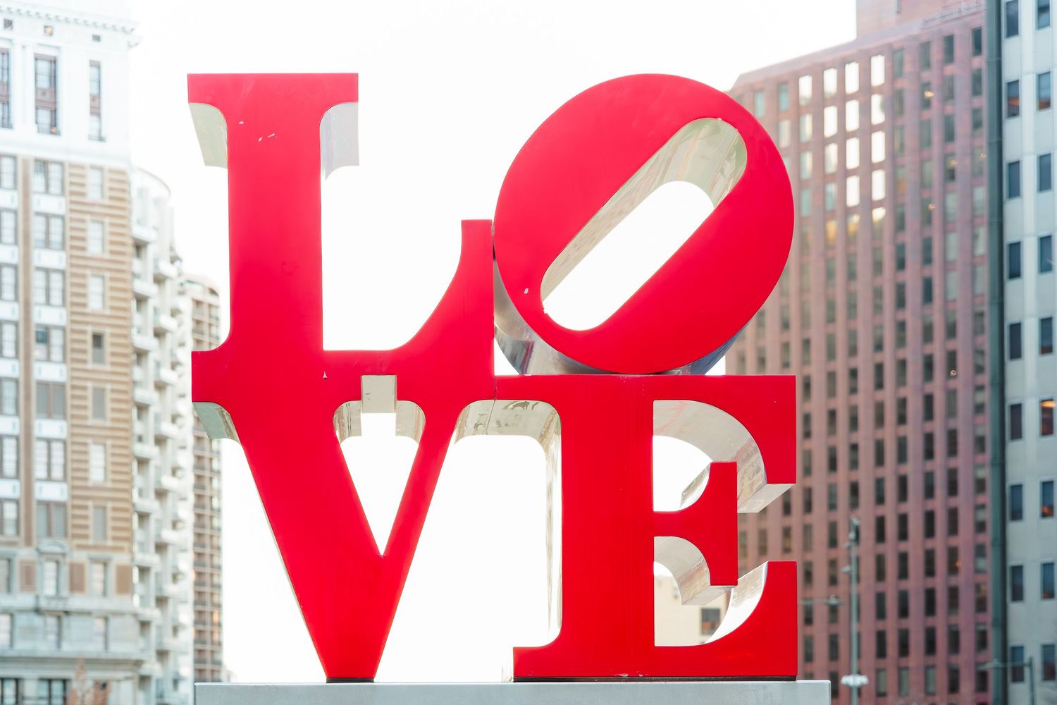 Iconic red LOVE sculpture by Robert Indiana displayed outdoors in Philadelphia with city buildings in the background.