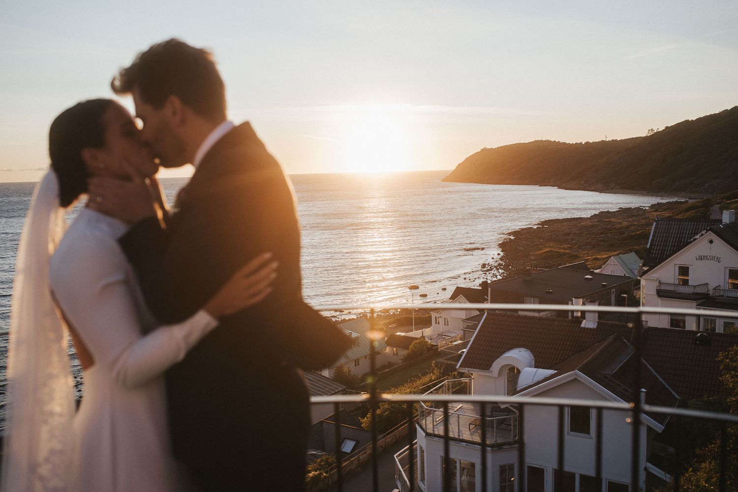 A couple in wedding attire poses romantically on rocky coastal cliffs overlooking the ocean.