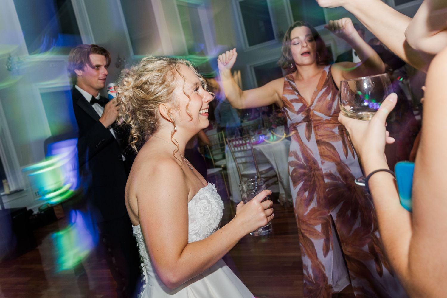 Wedding guests dance energetically under colorful party lights during an evening reception.