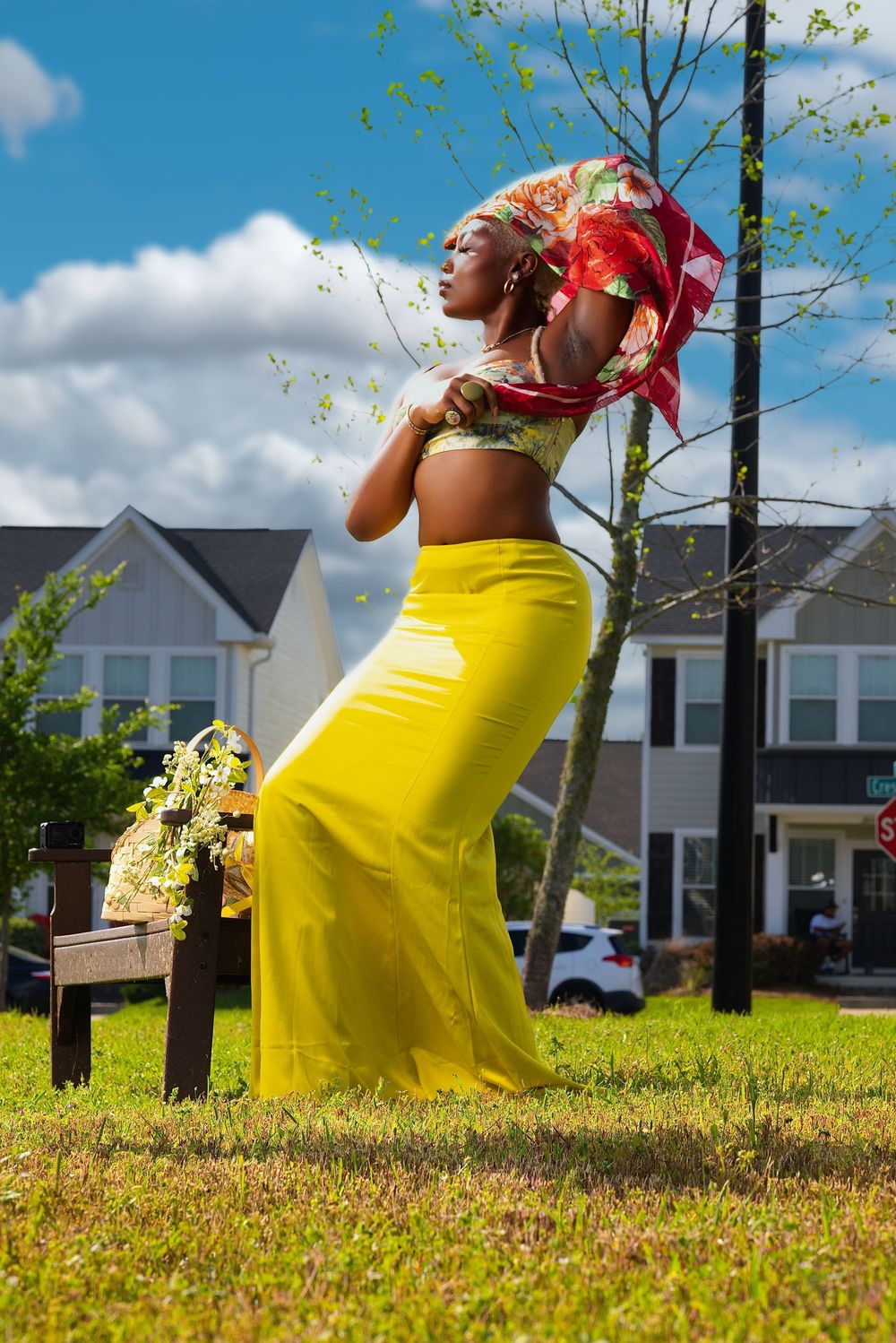 Person in yellow dress and red top relaxes on sunny grass with residential houses in background.