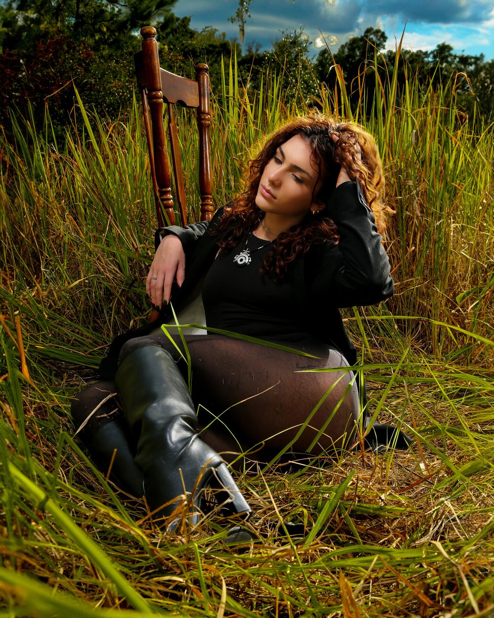 A figure in a black wetsuit lies among tall grass on a sunny day with dramatic clouds in the sky.