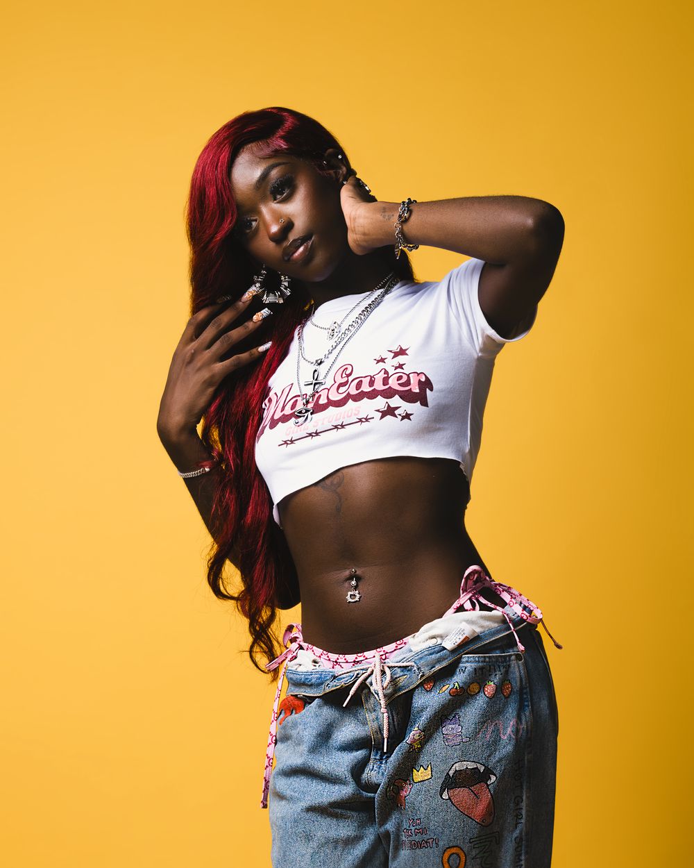 Fashion model in a cropped white t-shirt and embellished jeans poses against vibrant yellow background.