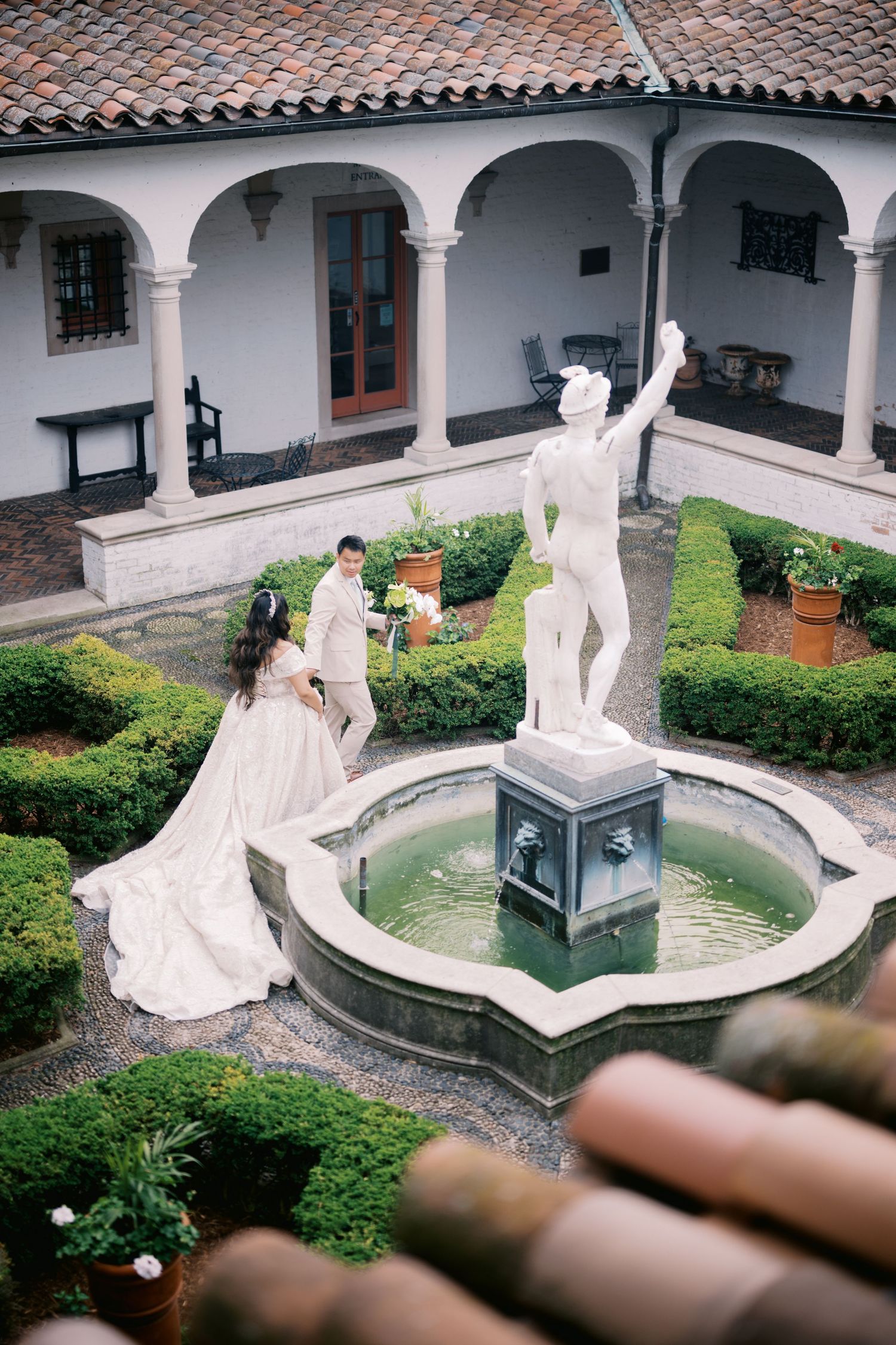 An elegant wedding scene in a Spanish colonial courtyard with arched walkways and a central fountain with white statue.
