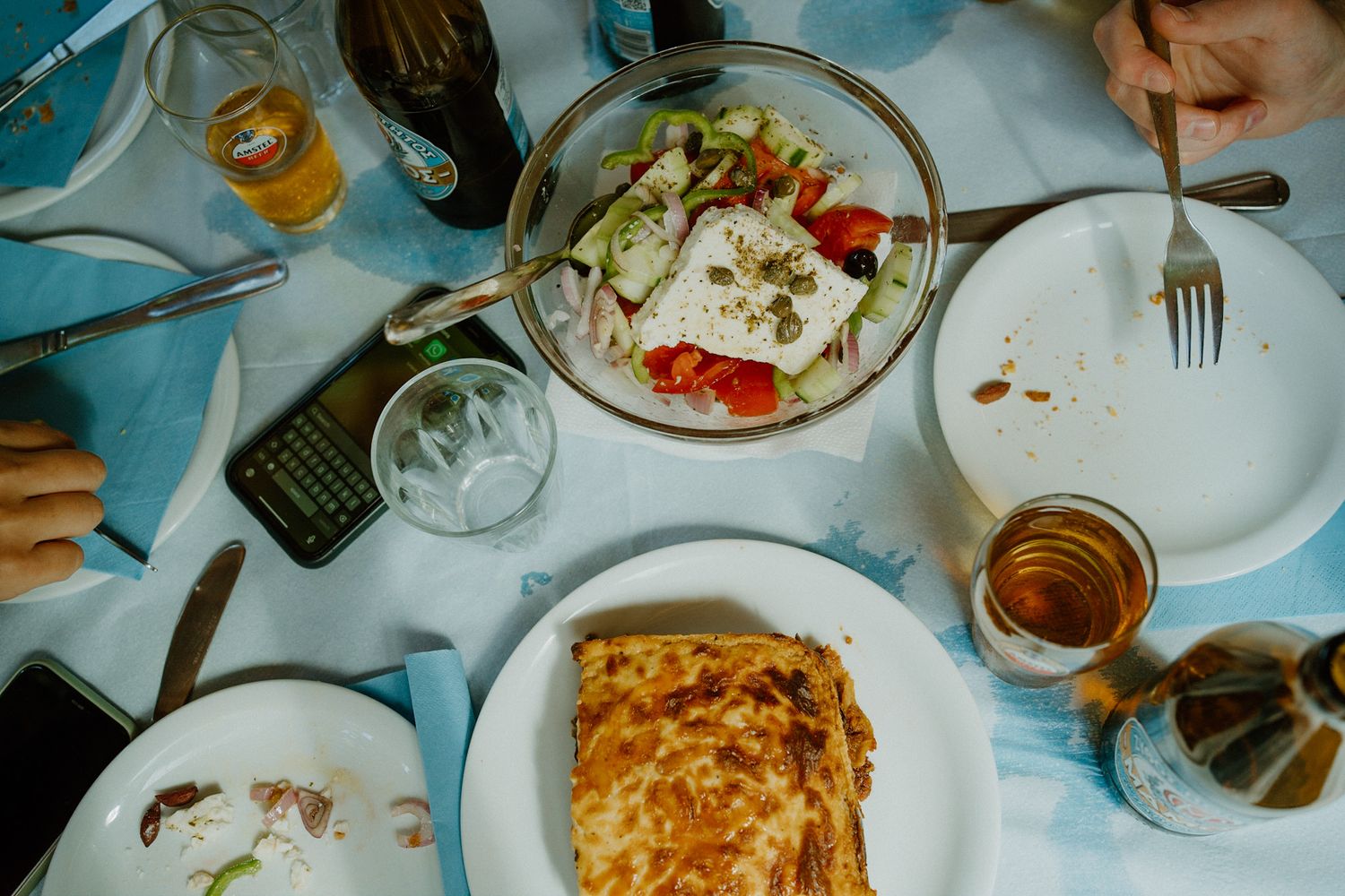 Overhead view of restaurant dining table with lasagna, salad plates, and drinks on a blue tablecloth.