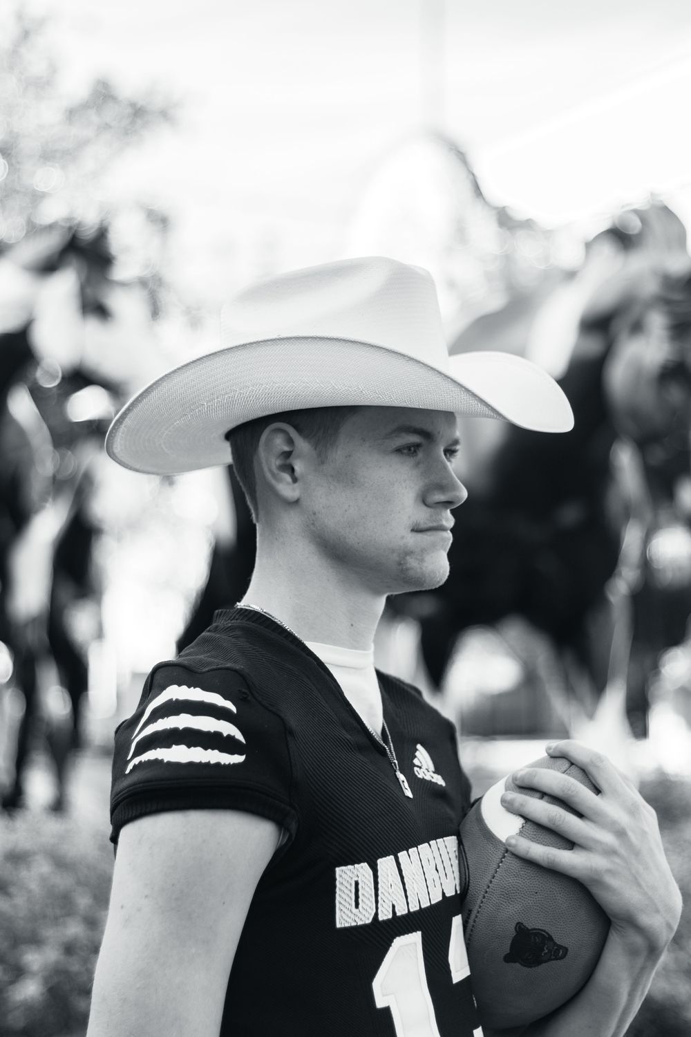 Black and white photo of a softball player in uniform wearing a cowboy hat while holding a ball.