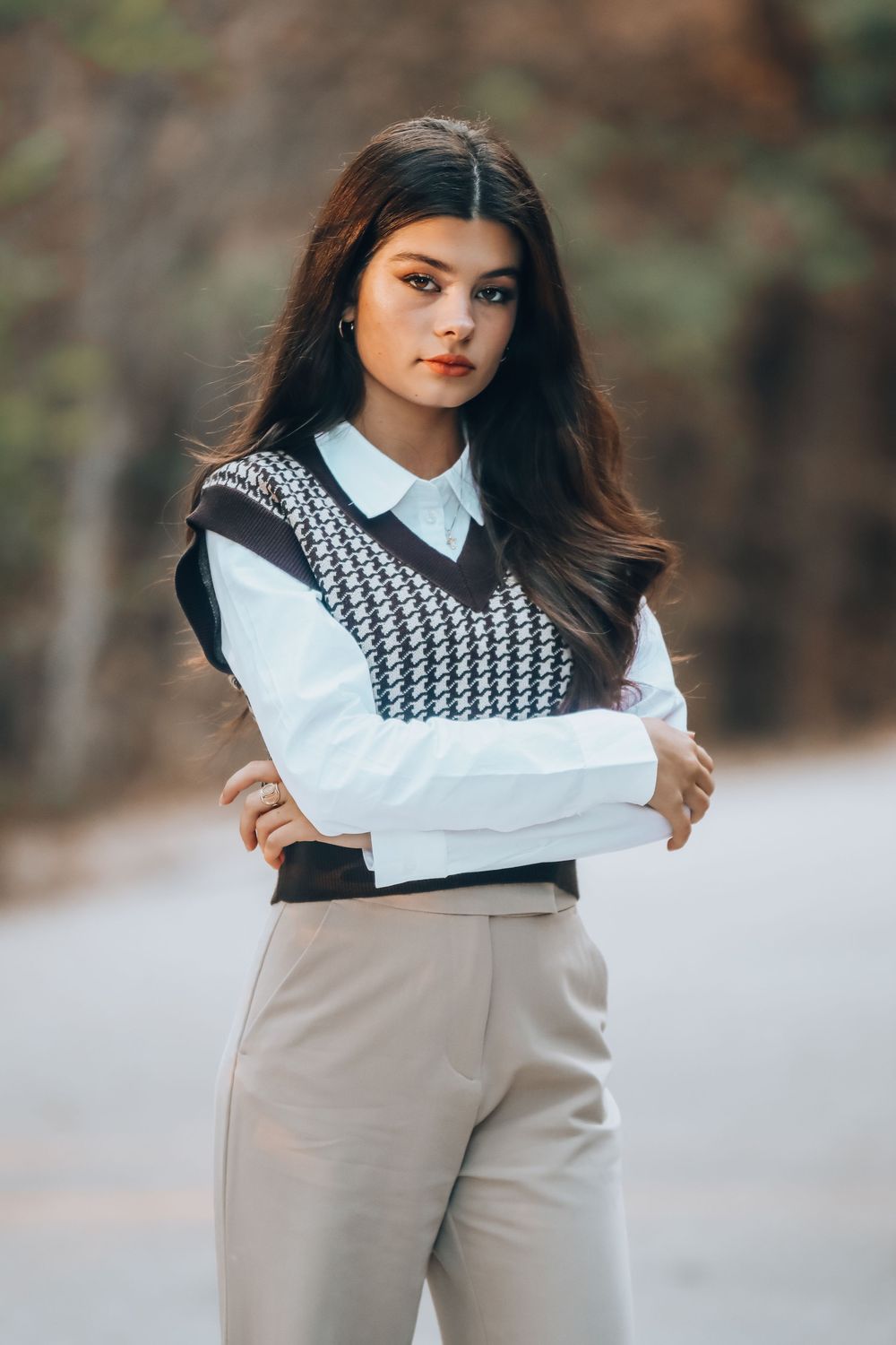 Fashion portrait featuring a houndstooth sweater vest layered over white button-down shirt with beige trousers.