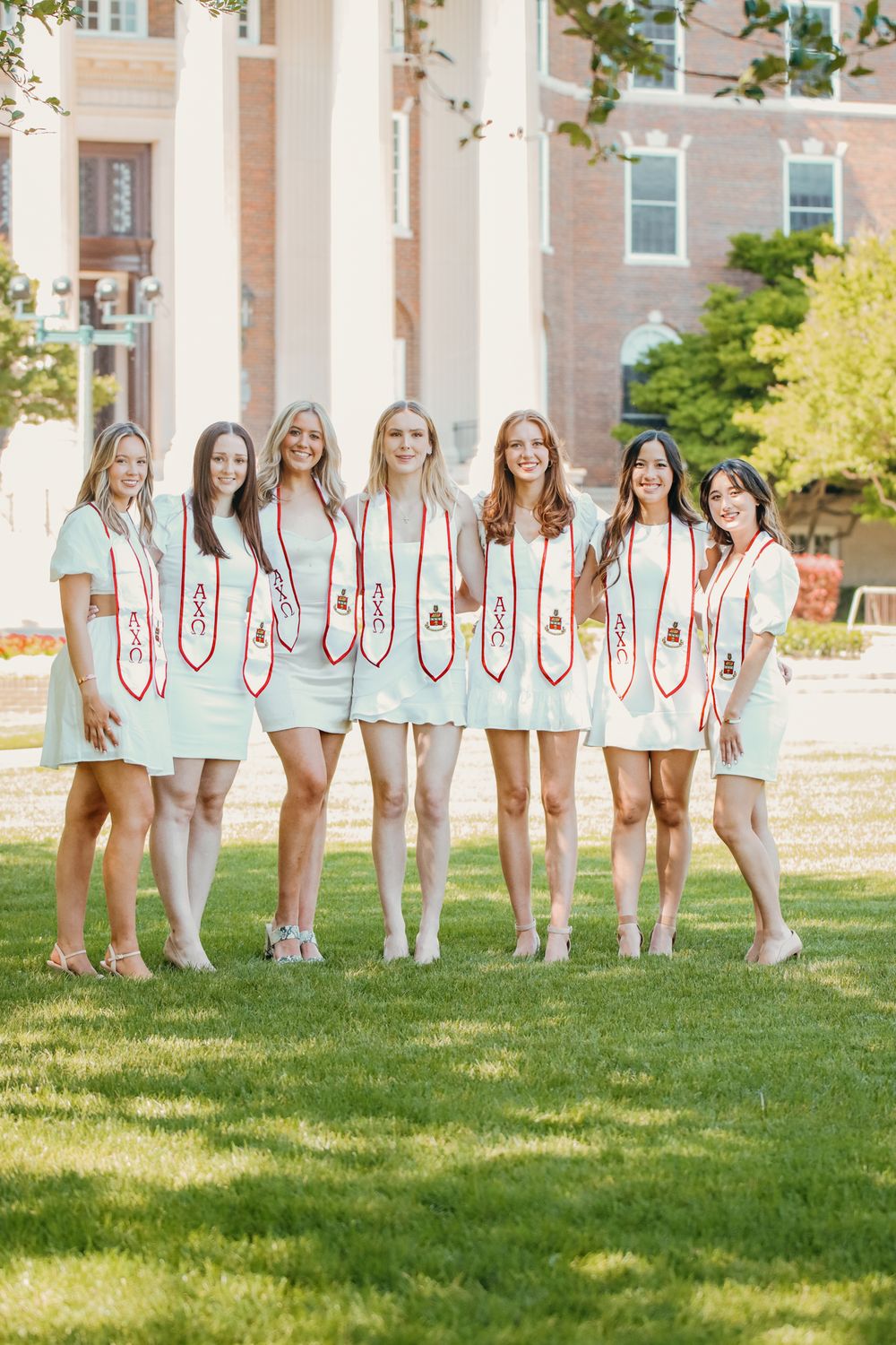 A group in matching light blue outfits poses together on a sunny lawn in front of a brick building.