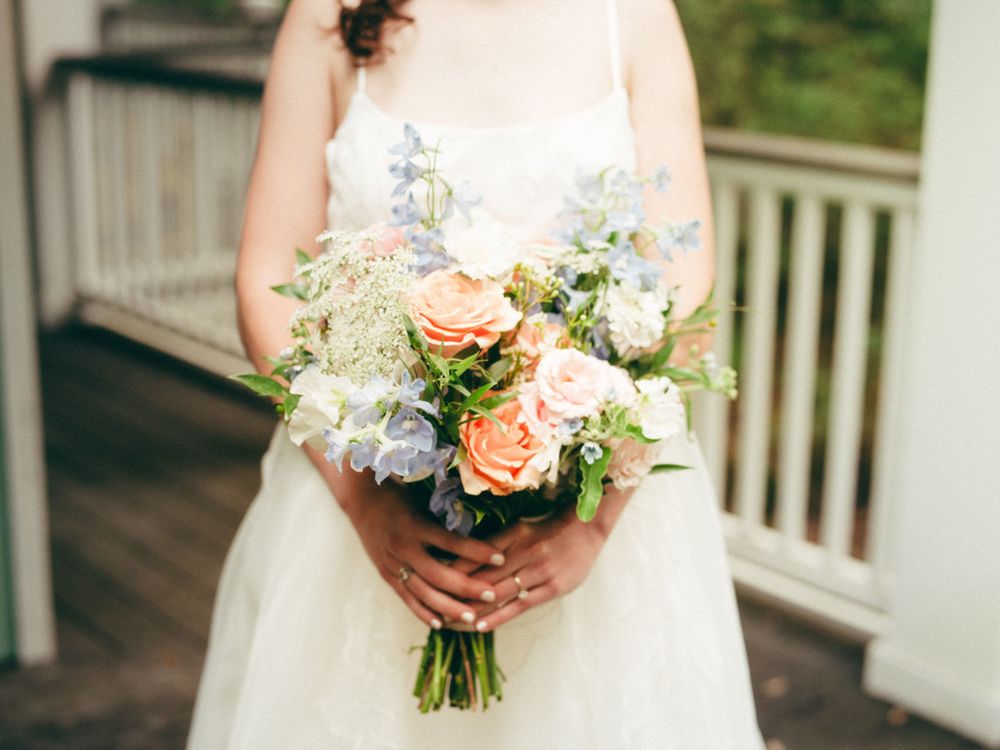 Close-up of a bridal bouquet featuring peach roses and blue hydrangeas against a white dress.