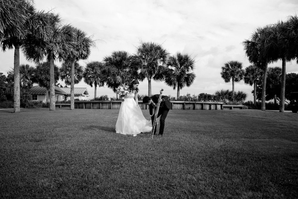 A couple standing on a grassy lawn surrounded by palm trees on a cloudy day during a wedding celebration.