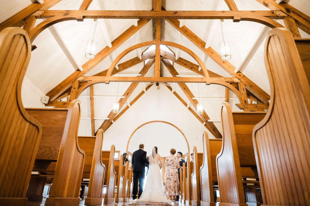 A wedding ceremony takes place in an elegant chapel with exposed wooden beams and vaulted ceilings.
