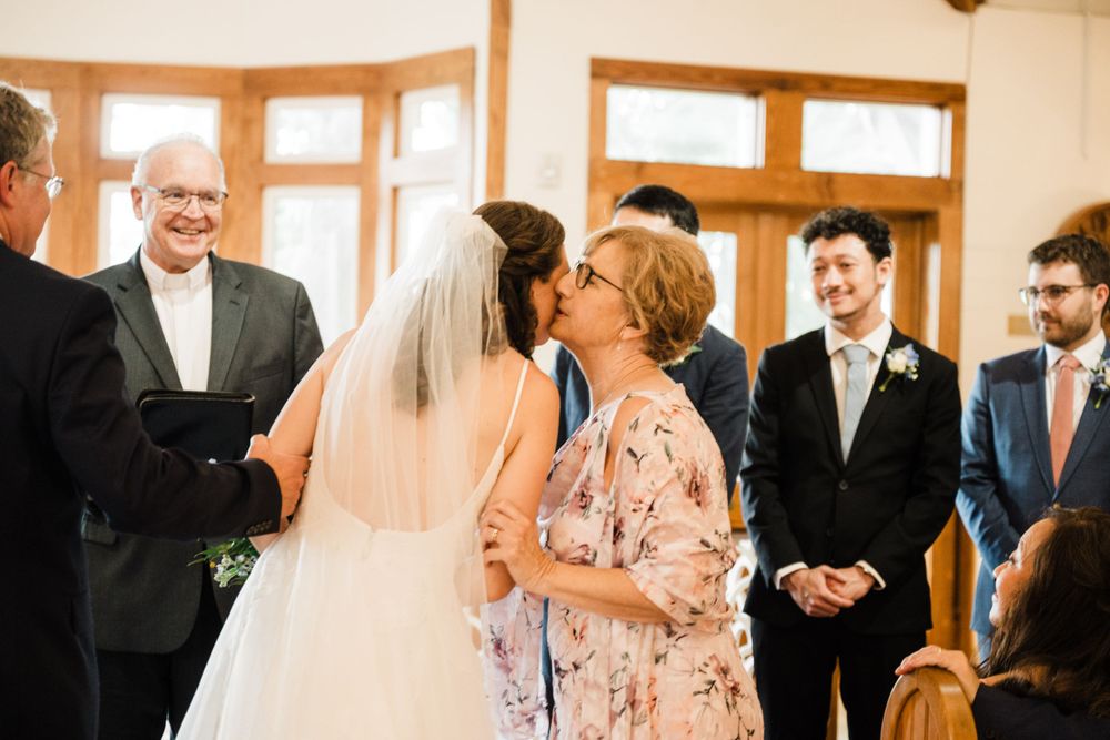 An emotional embrace during a wedding ceremony as guests look on inside a bright chapel setting.