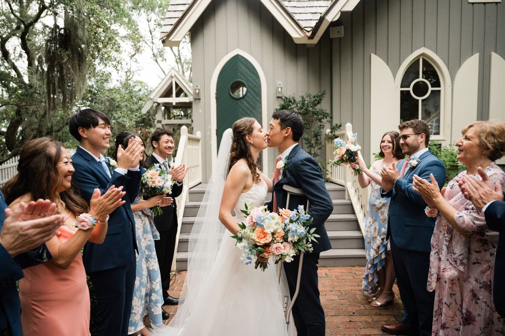 Wedding party celebrates with the newlyweds outside a charming chapel with gothic windows.