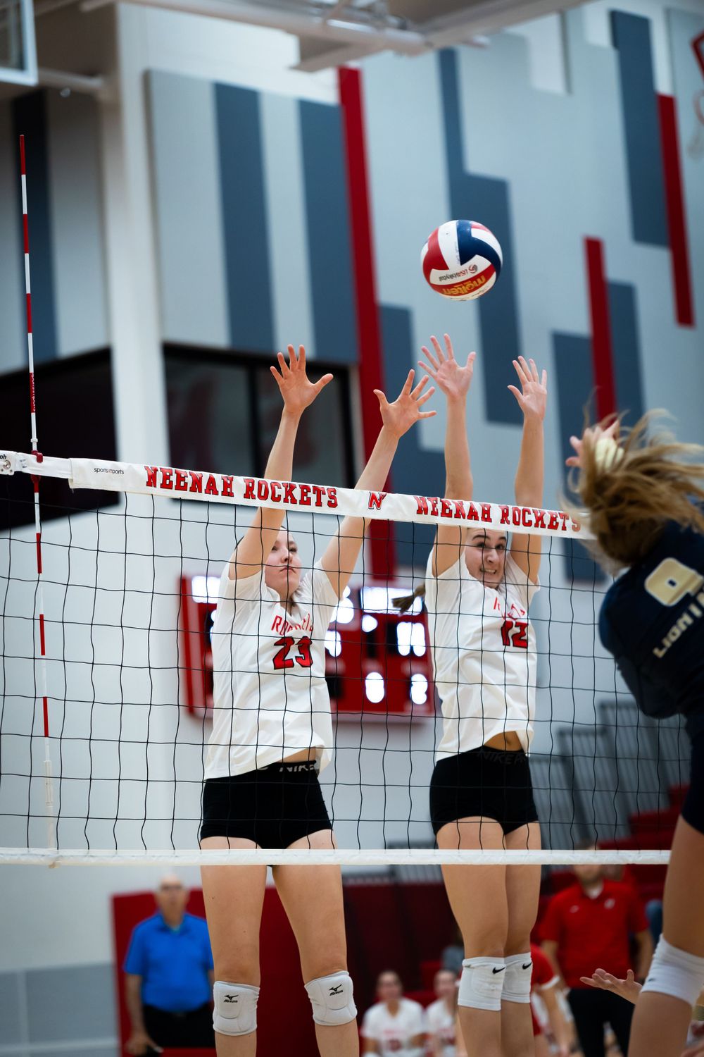 Two volleyball players jumping to block at the net during an indoor match.