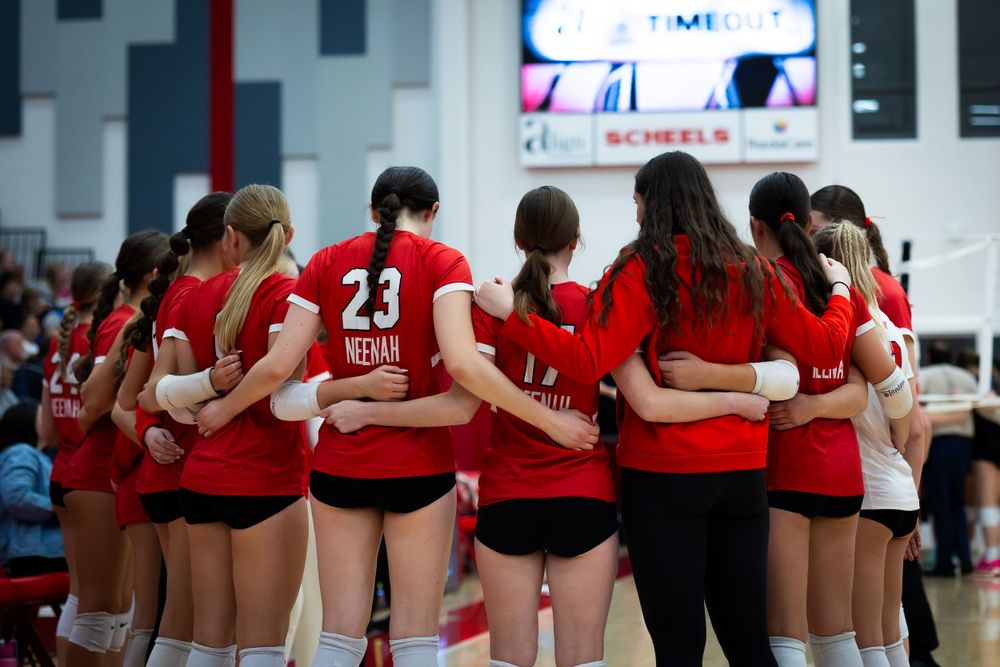 Team of volleyball players huddled together in red uniforms showing unity.