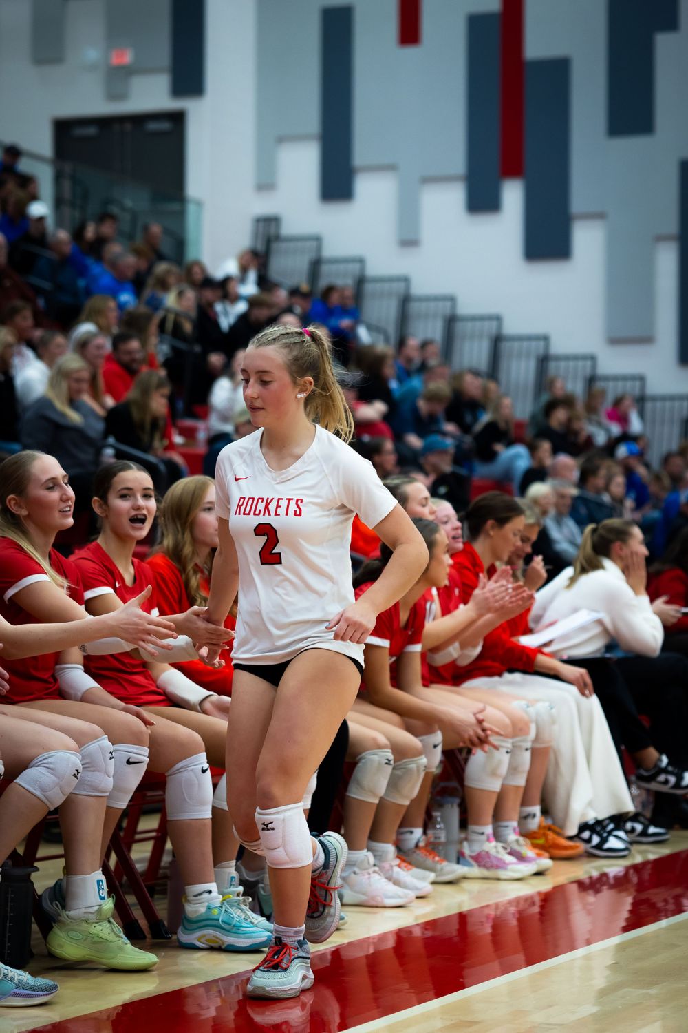 Volleyball players on sideline bench watching match in gymnasium.