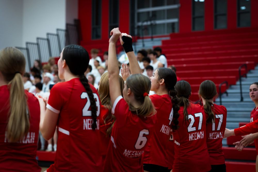 Volleyball team celebrating with raised arms during indoor match.