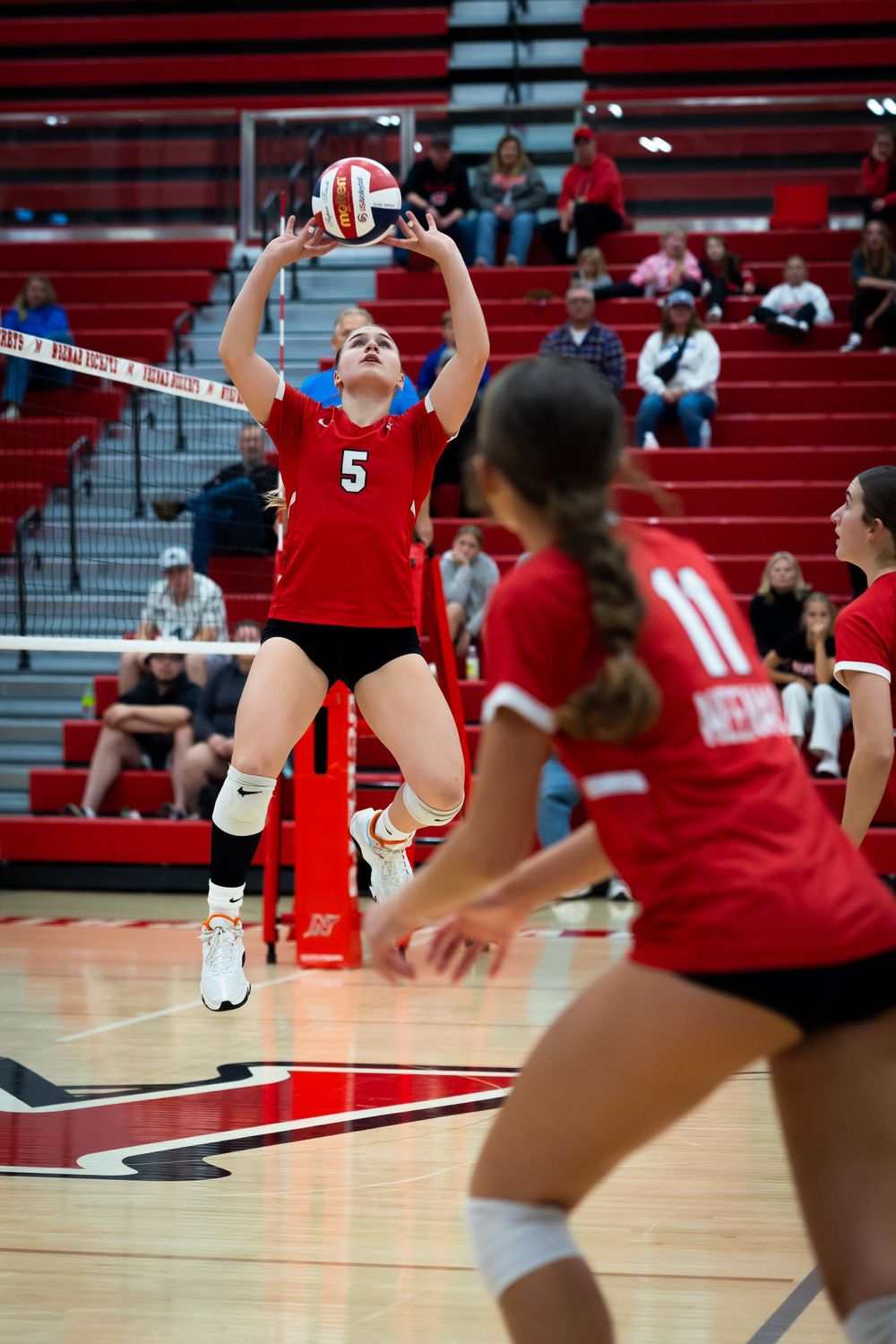Volleyball player in red jersey sets the ball during an indoor match on a court.
