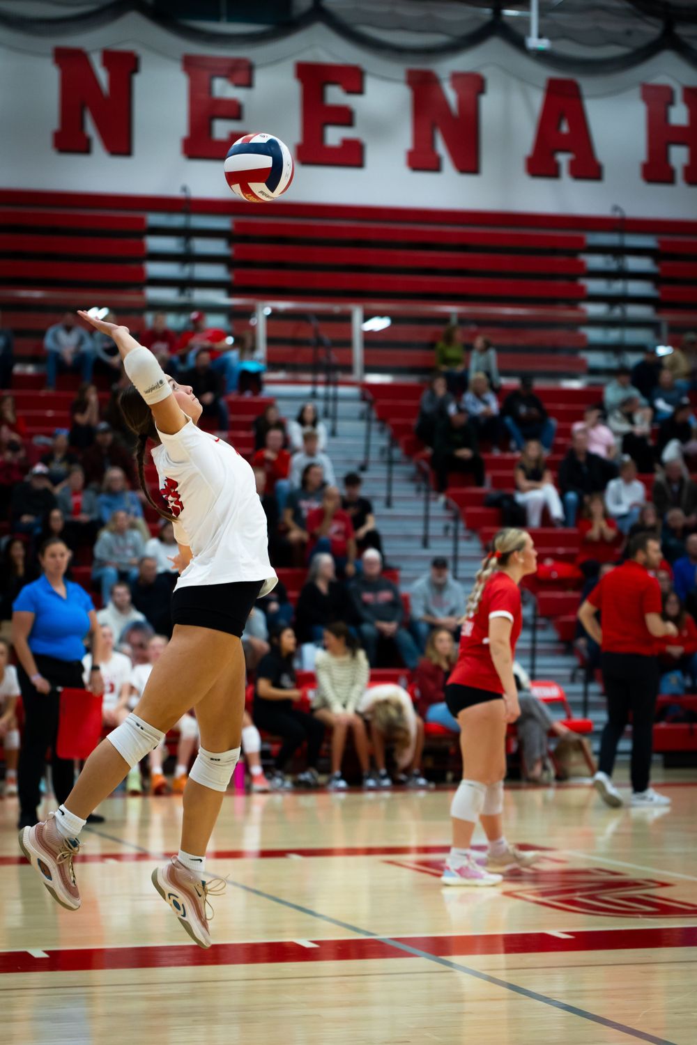 A volleyball player jumps to serve the ball in gymnasium.