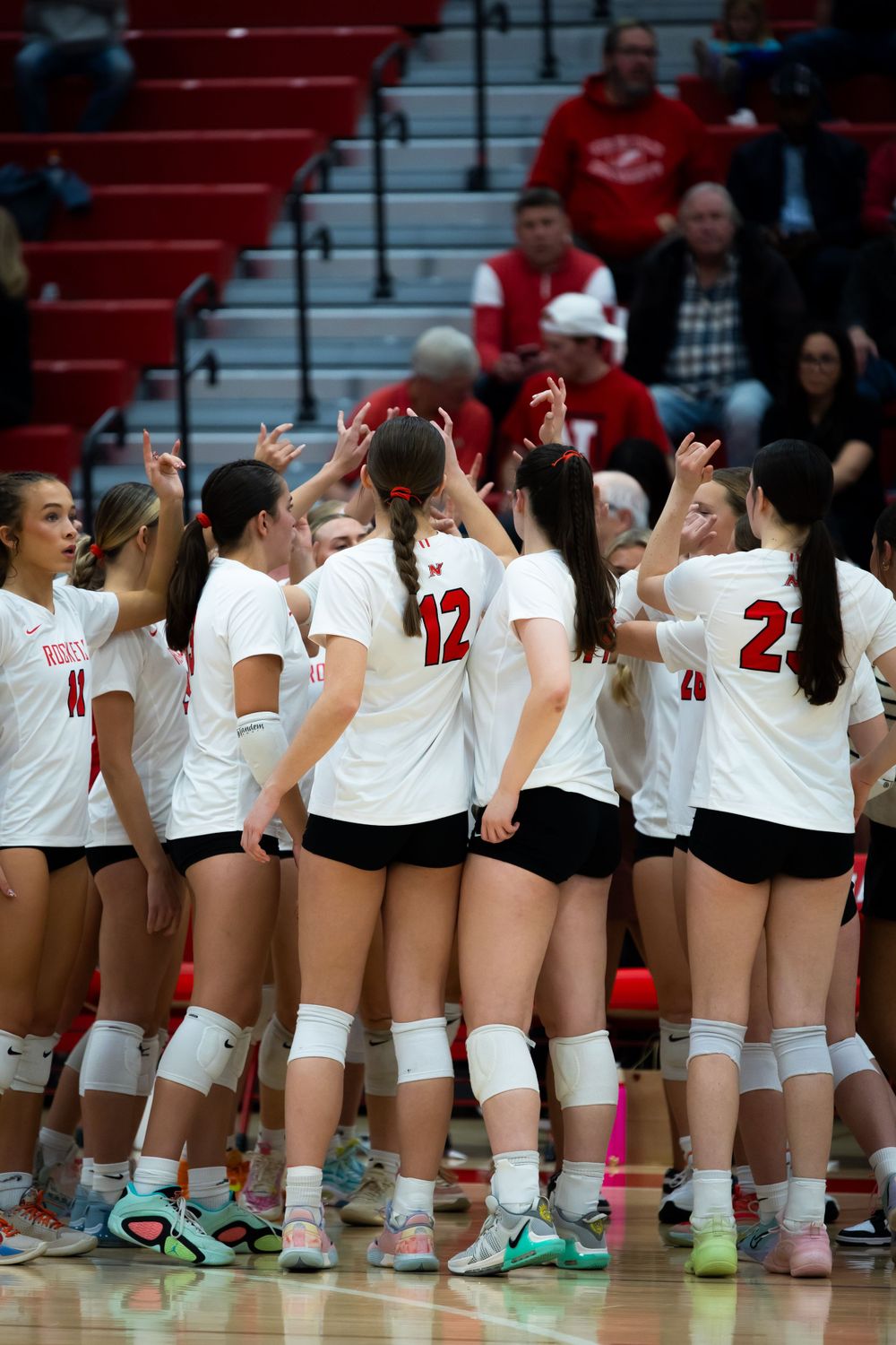 Volleyball team huddles together in white jerseys during a game.