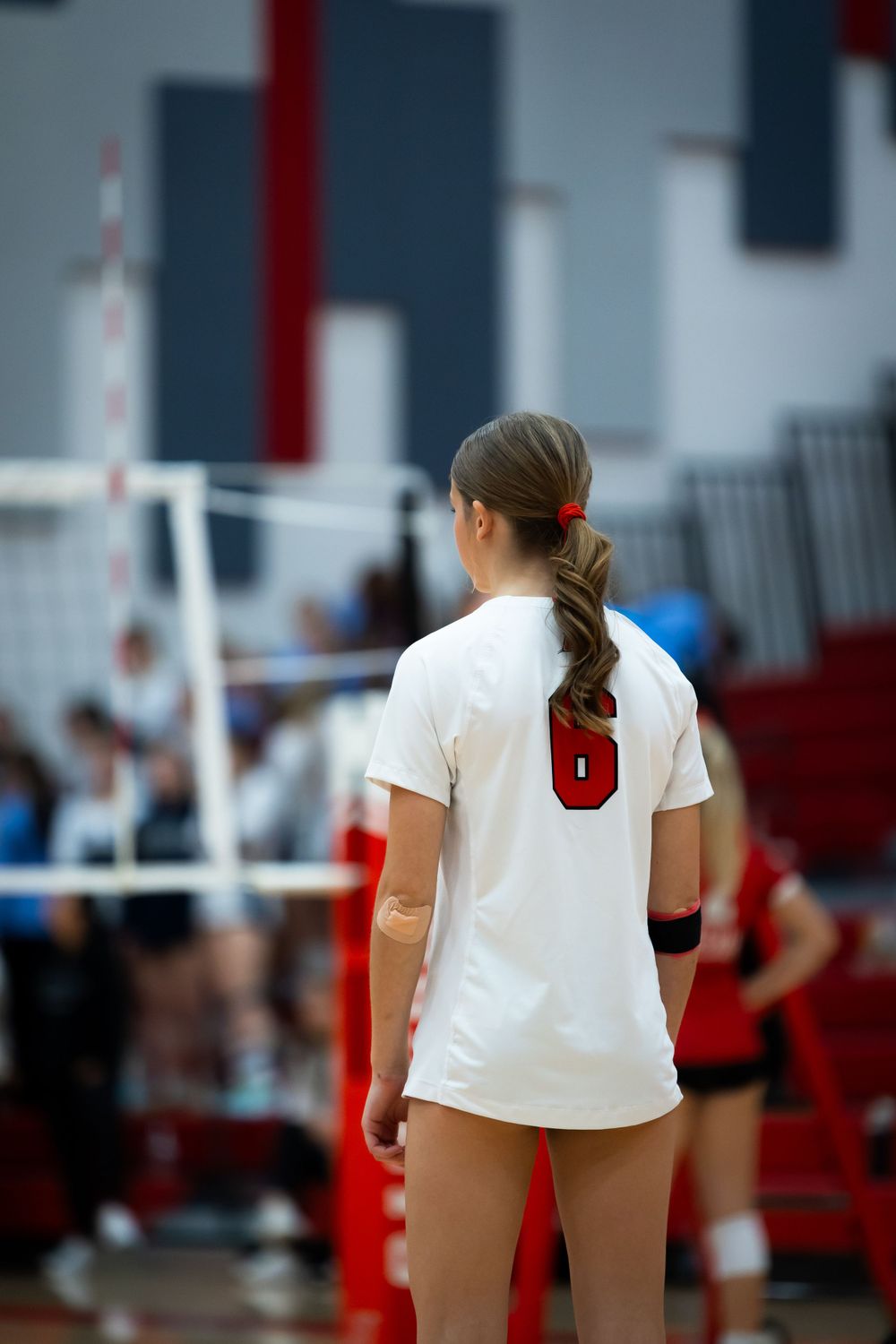 Volleyball player wearing white jersey stands ready on court.