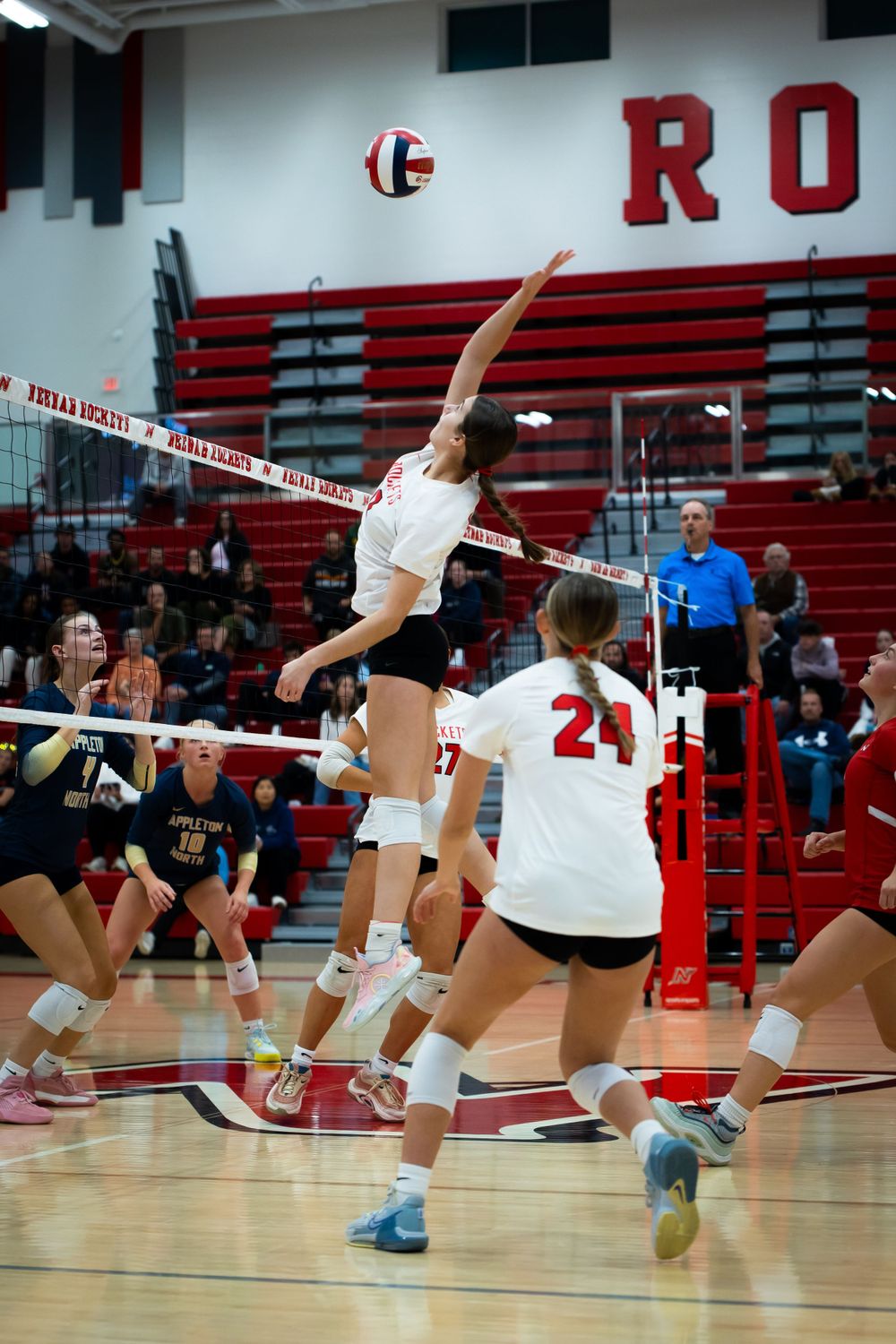 Player leaps high to hit volleyball during competitive indoor match.