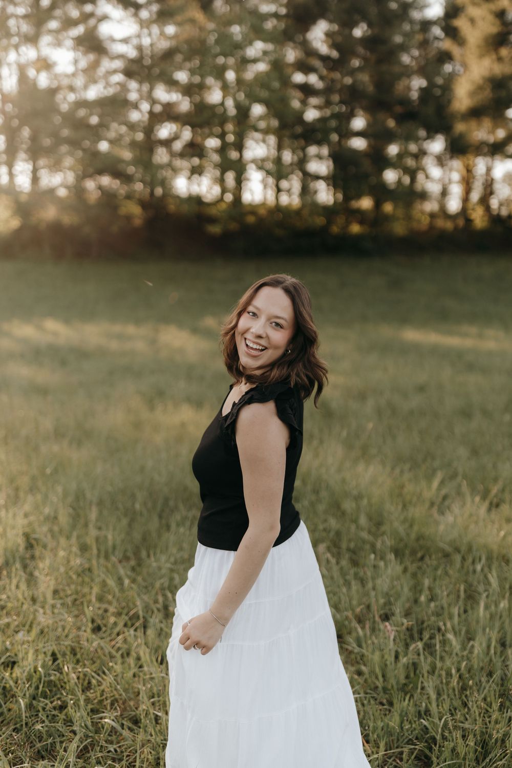 Joyful outdoor portrait of someone in black and white attire twirling in a sunlit meadow. Virginia graduation/senior session.