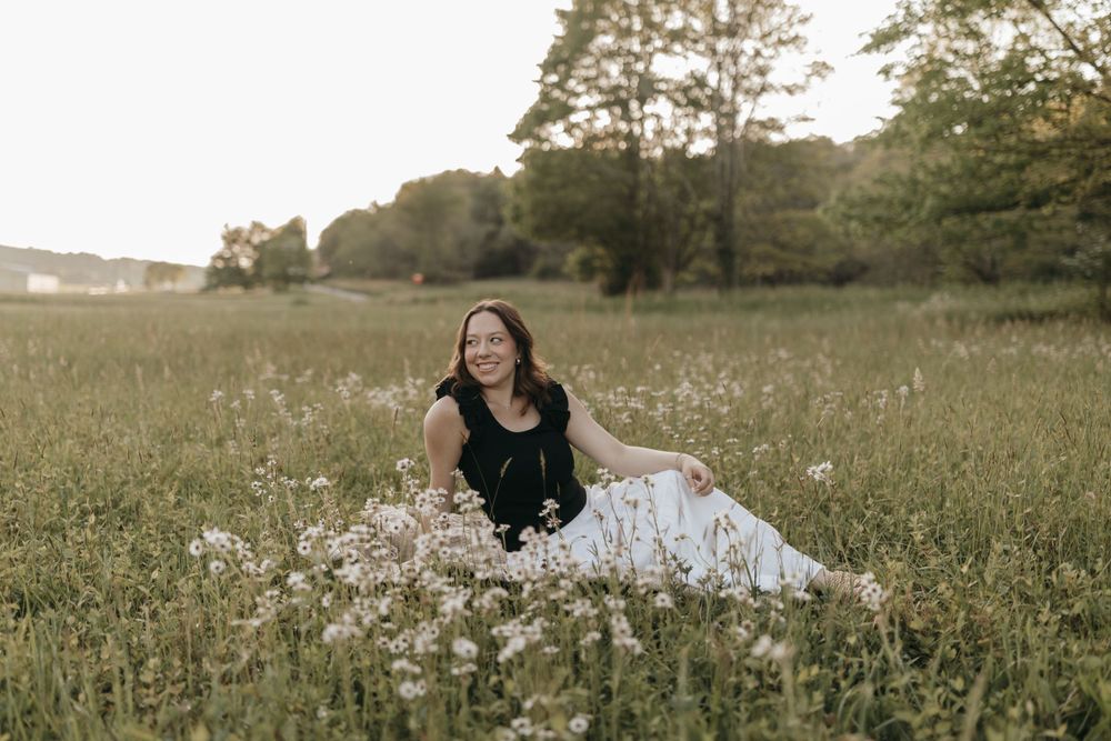A woman in contrasting black and white outfit sits amongst wildflowers in a serene meadow setting.  Virginia graduation/senior session.