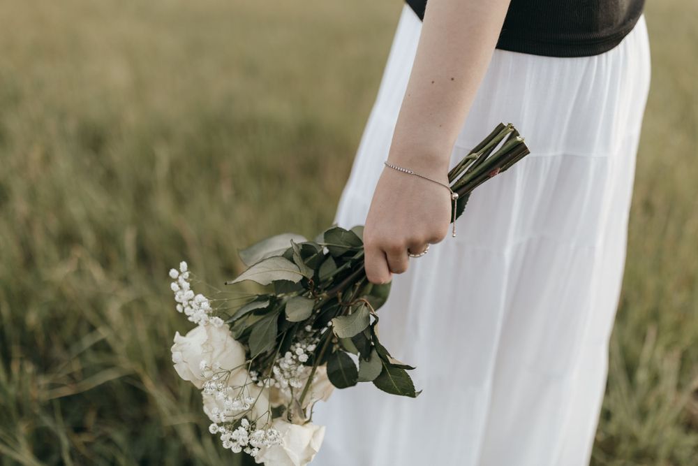 Close-up shot of hands holding a bouquet of white flowers and greenery against a flowing white skirt.  Virginia graduation/senior session.