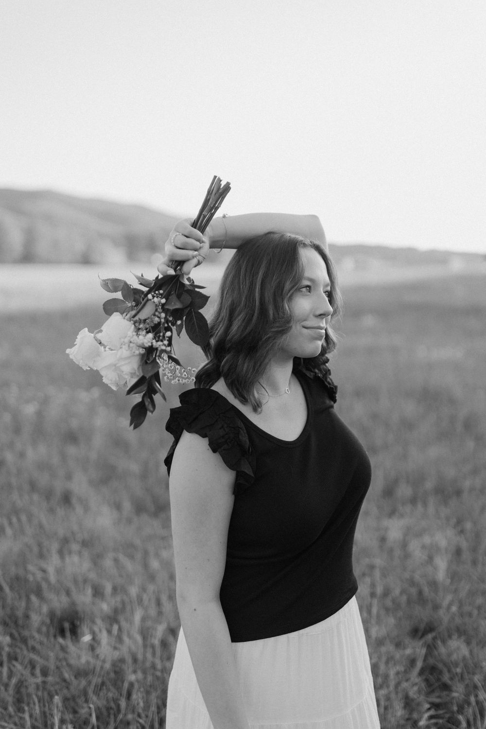 Black and white portrait of a woman in ruffled top holding flowers against mountain backdrop.  Virginia graduation/senior session.