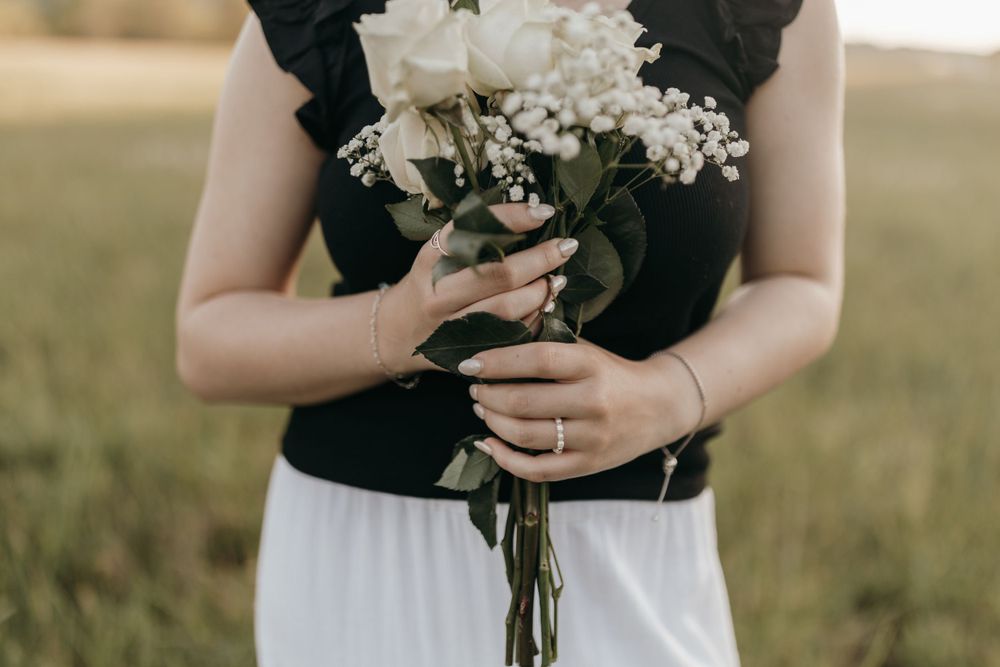 Person wearing black top and white skirt holds a beautiful bouquet of white flowers in a sunny field.  Virginia graduation/senior session.